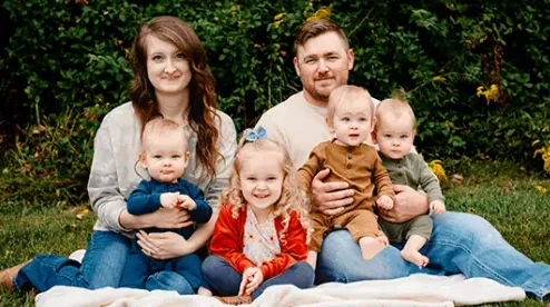 The Cravens Family poses on a blanket outside. Mom, Dad, little sister, and three baby triplets.