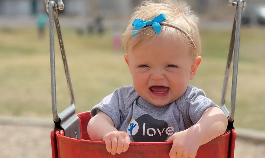 Toddler Ellie sits in a baby swing at the playground