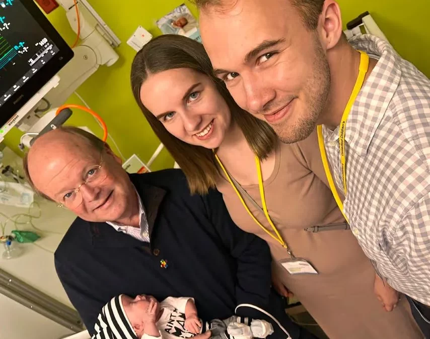 Dr. Crombleholme holds a new baby and smiles at the camera with two young parents.