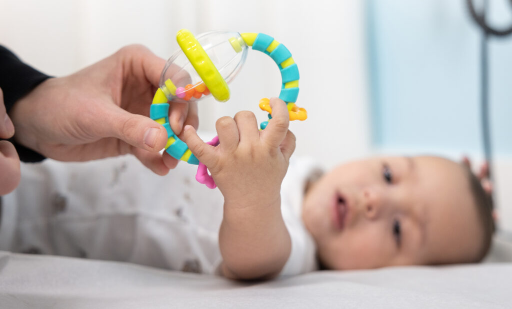 Baby grabs rattle while lying down