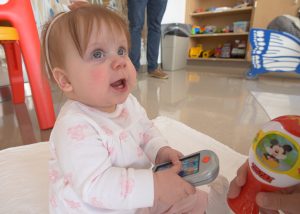 On-year-old baby plays with a remote control toy in a playroom