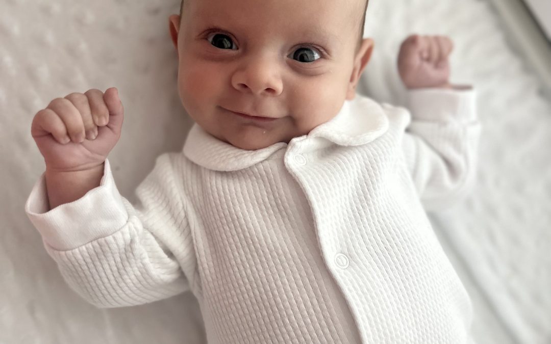 Bright-eyed infant lies in his crib, slightly smiling