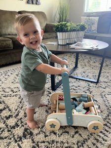 Toddler boy walks while pushing wheeled cart full of wooden blocks