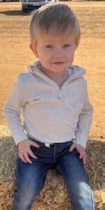 Toddler boy smiles and sists on haystack