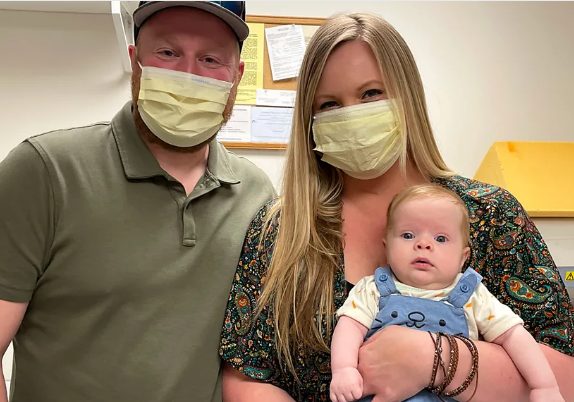 Mom and dad wearing medical face masks while mom holds baby boy