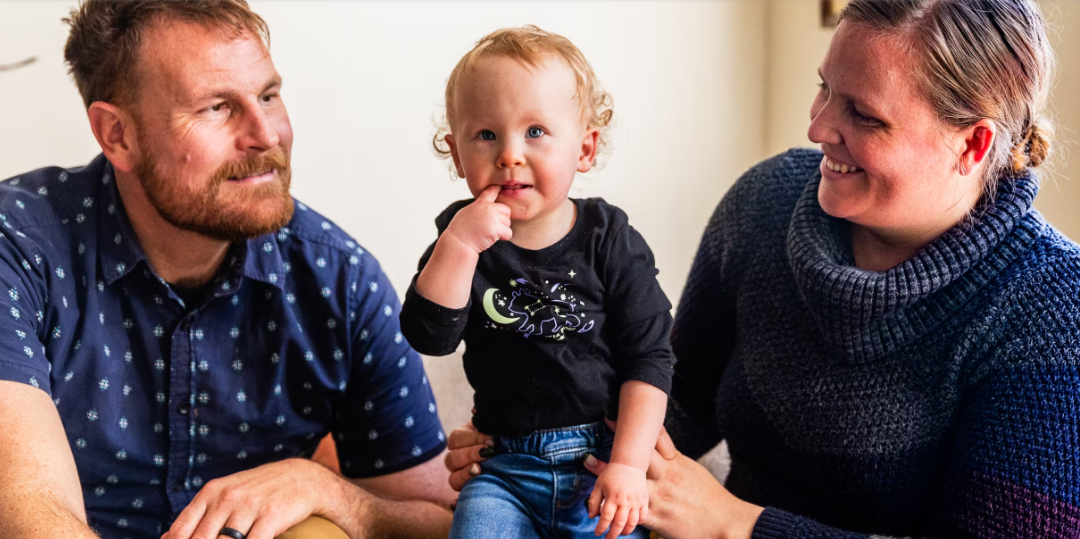 Mom and dad smile at one-year old daughter